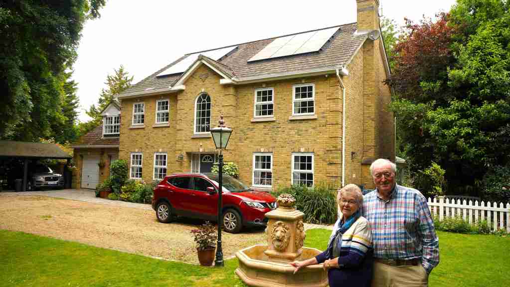 A married retired couple in front of their house in Brampton, Cambridgeshire with new solar panels fitted